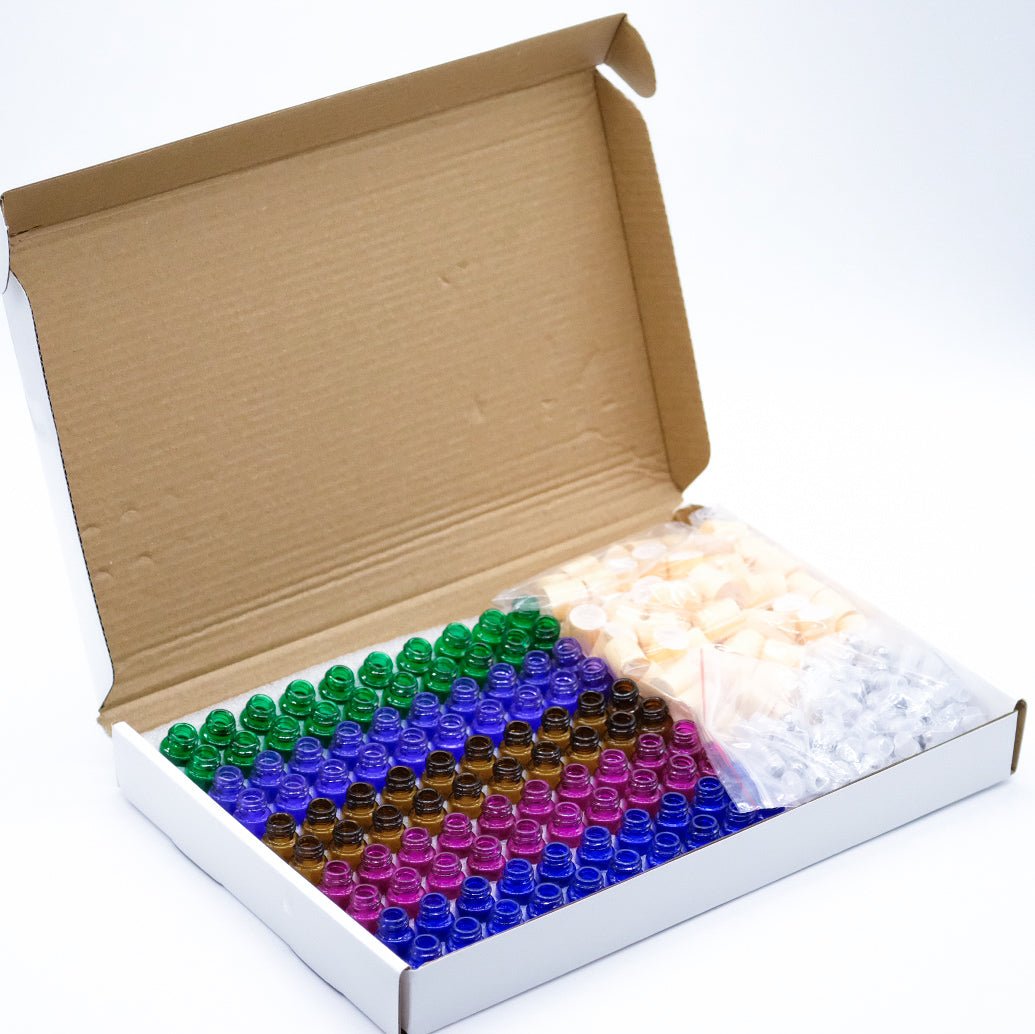 Kit de flacons vides pour huiles essentielles dans une boîte en carton ouverte. Comprend des mini flacons en verre coloré avec bouchons et applicateurs, idéal pour le mélange et le transport d'huiles essentielles.