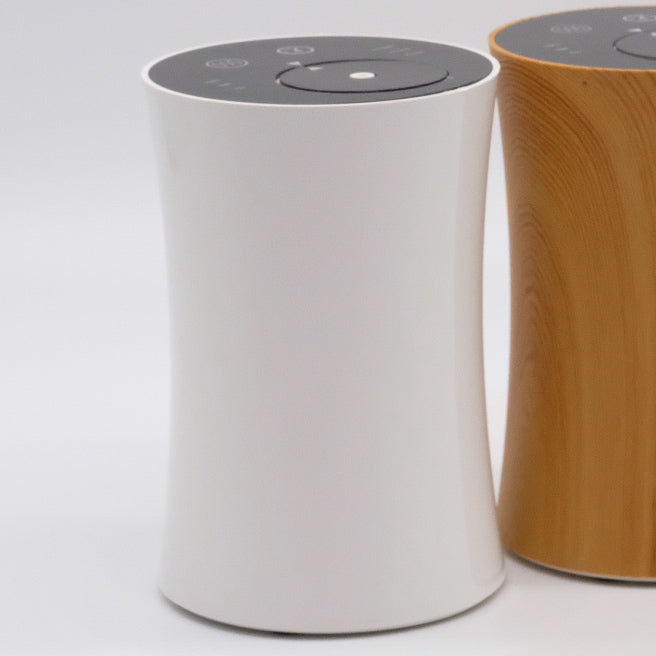 Nébulisateur blanc au premier plan, design courbé et panneau de commandes sur le dessus; modèle bois en arrière-plan.