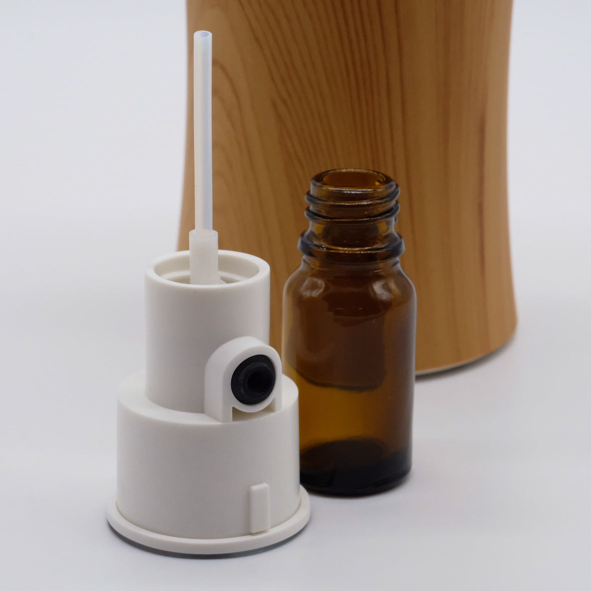 Tête de nébulisation blanche avec tube et adaptateur, bouteille ambrée ouverte, base effet bois en arrière-plan.